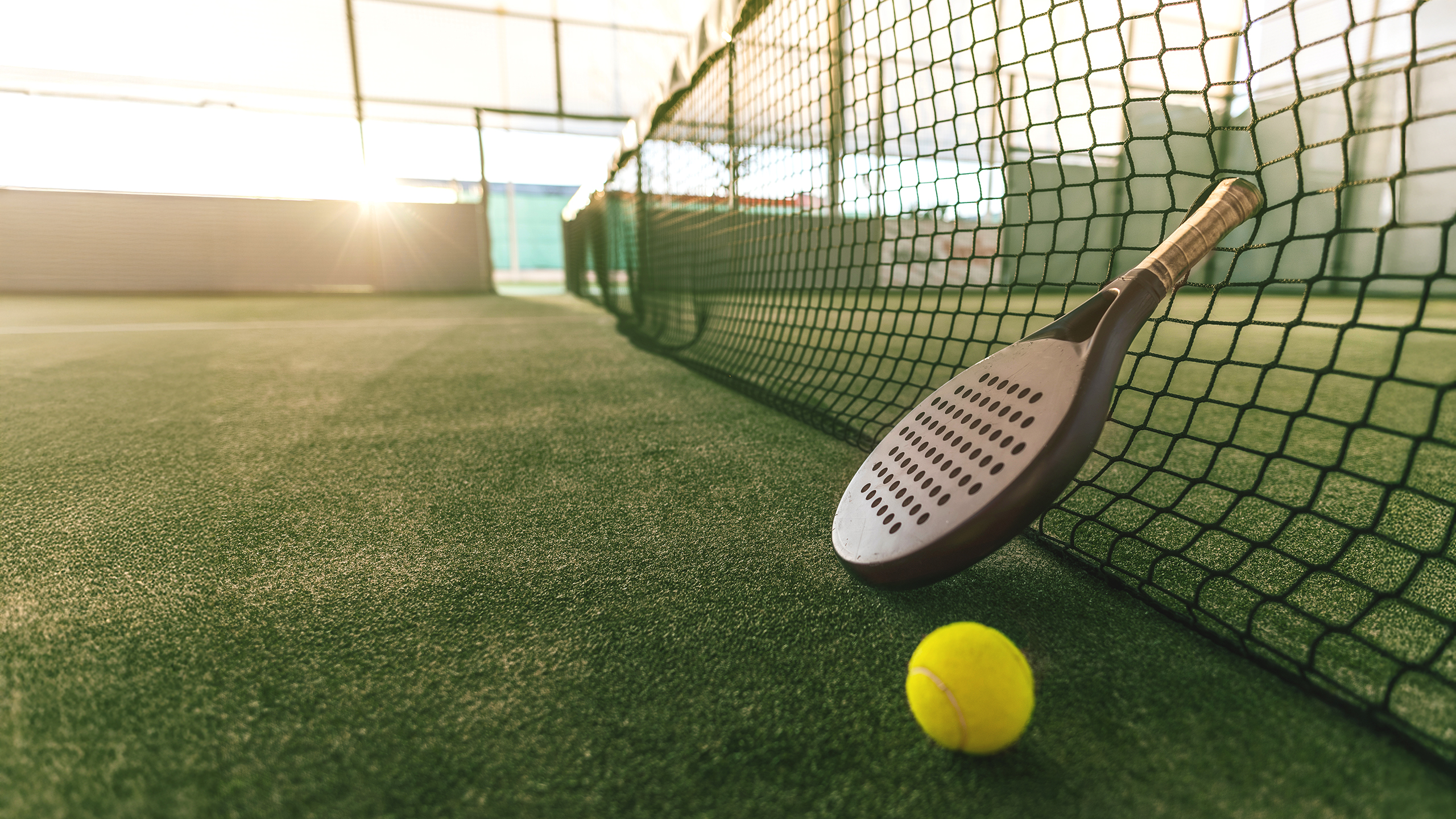 Padelschläger lehnt am Netz, daneben ein Ball